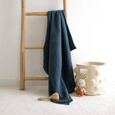 Navy blue 4-ply muslin baby blanket hanging on wooden ladder beside toy basket